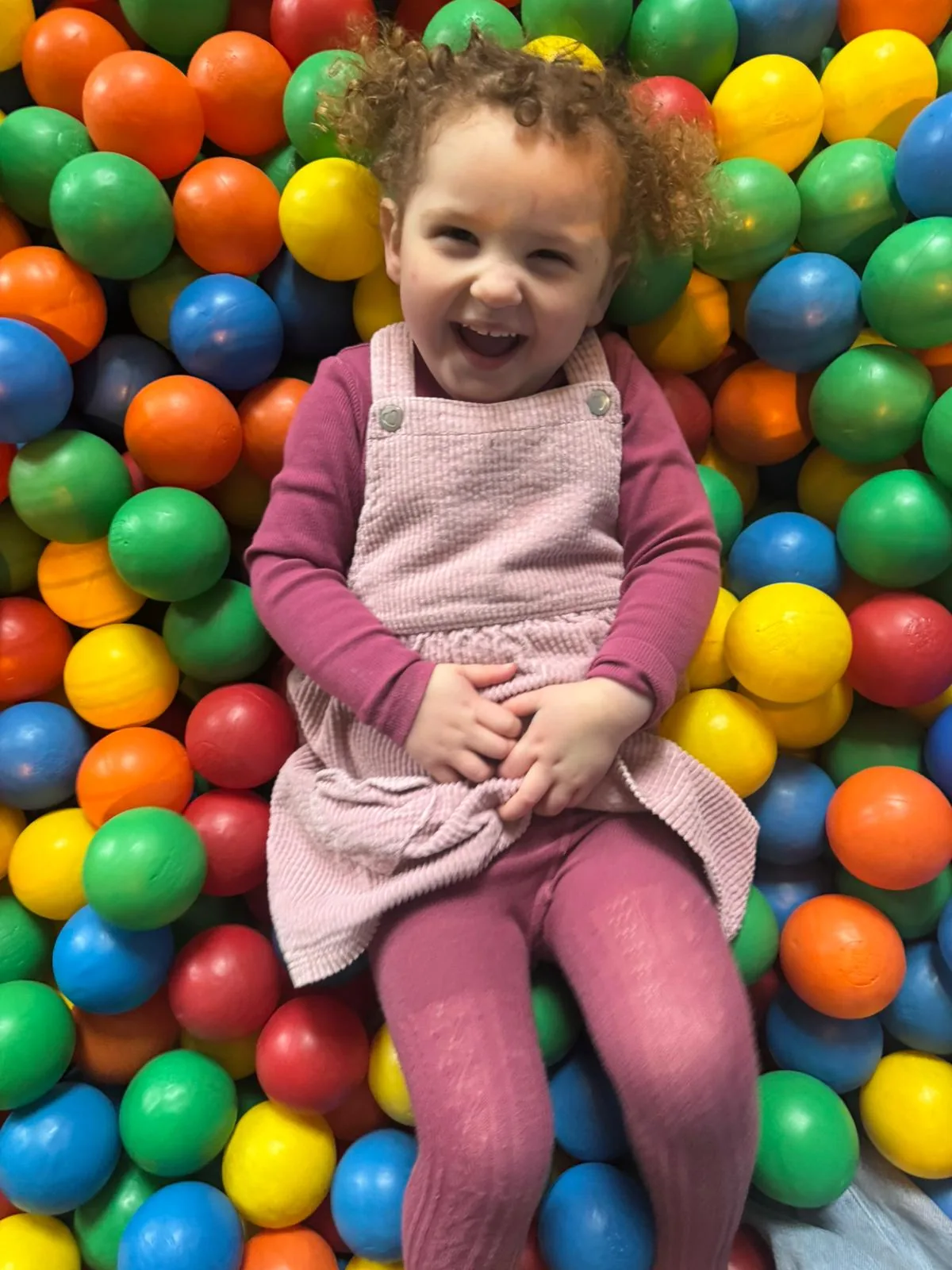 A little girl laughing in the ball pit